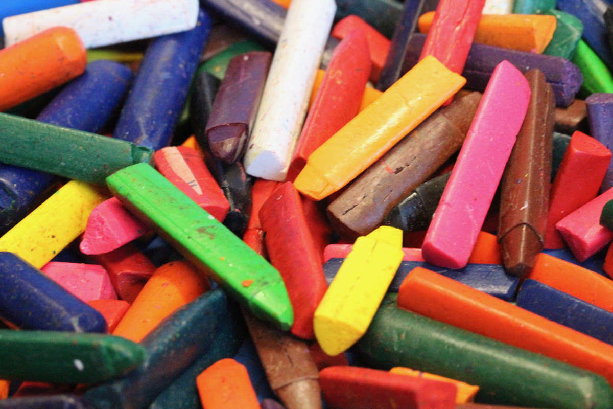 many colors of crayons strewn haphazardly in a blue plastic bin